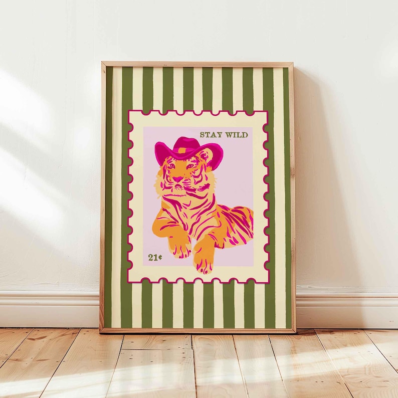 May include: Framed art print with a tiger wearing a pink cowboy hat, set on a pink background within a postage stamp design. The words "STAY WILD" are above the tiger. The frame has a green and white striped pattern.