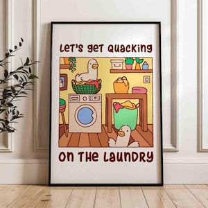 A colorful poster print of two ducks, or goose, doing the laundry. One is sitting in the dirty clothes basket and the other runs around.