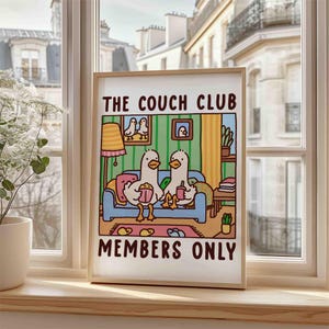 May include: A framed print with a cartoon illustration of two ducks sitting on a couch watching television. The print has the text "The Couch Club Members Only" at the bottom.