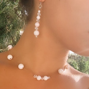 May include: A white pearl necklace and matching earrings. The necklace is a simple design with a single strand of pearls. The earrings are long and dangle, with a single pearl at the bottom.