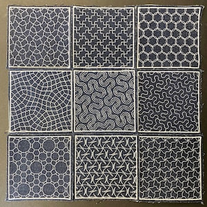 Puede incluir: Nueve parches cuadrados de tela con varios patrones geométricos blancos bordados sobre un fondo azul oscuro. Los diseños incluyen círculos entrelazados, líneas onduladas y formas de cruz. Cada parche está delineado con un borde blanco.