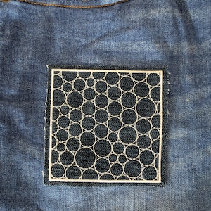 May include: A blue denim patch with a white embroidered design of overlapping circles.