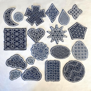 Op de afbeelding: Een verzameling van 16 zwarte en witte geborduurde patches met verschillende geometrische en abstracte ontwerpen. De patches zijn allemaal in verschillende vormen en maten, en ze zijn allemaal genaaid op een witte stoffen achtergrond.