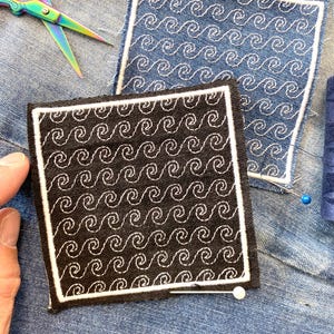 May include: Two square patches with embroidered wave patterns. One patch is black with white stitching, the other is denim blue with white stitching. A pair of rainbow scissors and pins are also visible.