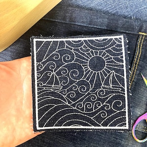 Puede incluir: Parche cuadrado azul marino con un diseño bordado en blanco de un sol, veleros y olas del océano. El parche tiene un borde blanco y es para coser en ropa o accesorios.