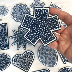 Könnte beinhalten: Eine Sammlung von blauen und weißen gestickten Aufnähern in verschiedenen Formen, darunter ein Stern, ein Herz, ein Quadrat und ein Kreis. Die Aufnäher zeigen komplizierte geometrische und florale Muster.