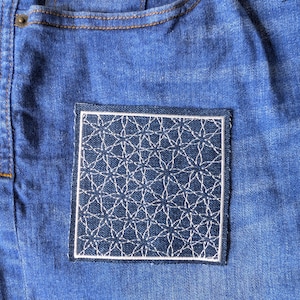 May include: A white embroidered patch with a geometric pattern on a blue denim background.