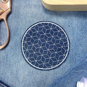 Pode incluir: Um remendo bordado branco com um design geométrico em um fundo de jeans azul.