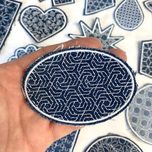 Op de afbeelding: Een verzameling blauwe en witte geborduurde patches in verschillende vormen, waaronder een hart, een ster, een traan, een zeshoek en een cirkel. De patches zijn gemaakt van denim stof en hebben een witte omtrek.