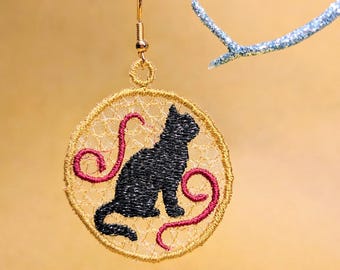 May include: Embroidered cat earring with a gold-colored filigree design. The black cat is seated, with red swirls. The earring hangs from a gold-colored hook. The background is a solid, light-yellow color.