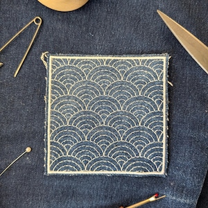 May include: A square, blue denim patch with a white, embroidered wave pattern. The patch is surrounded by sewing tools, including a seam ripper, pins, and scissors. The patch is approximately 7.6 cm by 7.6 cm.