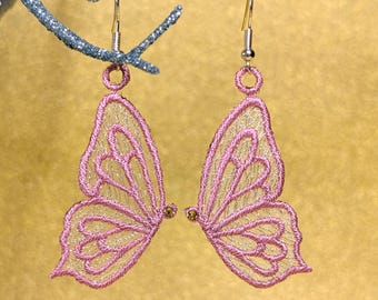 May include: A pair of pink butterfly earrings with gold-colored accents. The earrings are made of a delicate, embroidered material, and are suspended from silver-colored hooks. The earrings are displayed against a gold background.