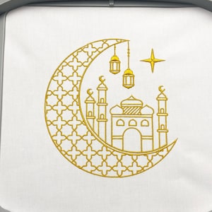 Puede incluir: Diseño bordado en oro de una luna creciente con un patrón geométrico, una mezquita con minaretes y tres linternas colgantes. Una estrella está por encima de la luna.
