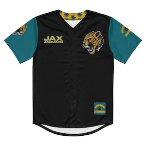 Może przedstawiać: Czarna koszulka baseballowa z turkusowymi rękawami. Koszulka ma napis "JAX JAGUARS" i grafikę głowy jaguara. Ma zapięcie na guziki z przodu i wzorzysty kołnierz. Rękawy mają logo.