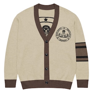 May include: Beige cardigan with brown trim and buttons. The sweater has a design on the left chest that says "EXPLOSIVE ORDNANCE DISPOSAL" and stripes on the left sleeve. The inside collar has a star and emblem design.