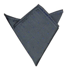 Puede incluir: Un pañuelo de bolsillo gris doblado en forma triangular con lunares azules. Los bordes están cosidos con hilo blanco. La tela tiene una textura. El fondo es blanco.