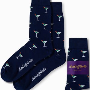 May include: Navy blue socks with a repeating pattern of white martini glasses with green olives and red garnishes. The brand name "AusCufflinks" is printed in white on the socks.