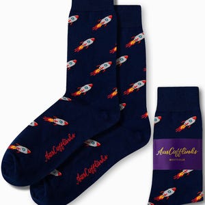 Peut inclure: Une paire de chaussettes bleu marine avec un motif de fusée. Les chaussettes sont emballées avec une étiquette qui dit "AusCufflinks Australia".