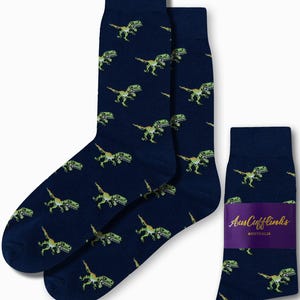 May include: Navy blue socks with a repeating pattern of pixelated green dinosaurs. The socks are displayed with a purple label that reads "AusCufflinks AUSTRALIA".