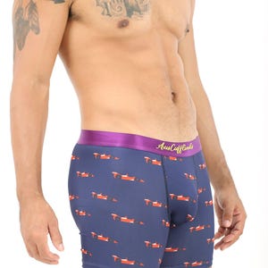 May include: Navy blue boxer briefs with a pattern of orange and white race cars. The waistband is purple with the text "Aus Cufflinks" in gold. The briefs are made of a soft, stretchy material.