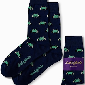 May include: A pair of navy blue crew socks featuring a repeating pattern of small, pixelated green alien creatures. The socks include the text AusCufflinks Australia printed on a purple band around one sock and on the fabric of the other.
