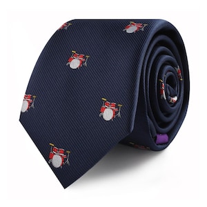 May include: A navy blue tie featuring a repeating pattern of red and white drum kits. The tie is rolled, revealing the pattern on the inside. The drum kits have yellow detailing.