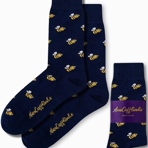 May include: A pair of navy blue socks with a yellow bee pattern. The socks are packaged with a purple and white label that says "AusCufflinks AUSTRALIA".