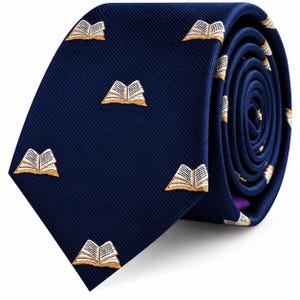 Peut inclure: Une cravate bleu marine foncé ornée d'un motif brodé répétitif de livres ouverts. Les livres présentent des pages blanches et des couvertures dorées, contrastant avec la texture côtelée en diagonale du tissu de la cravate enroulée.