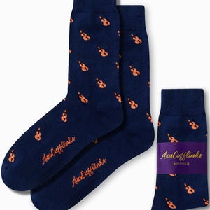 May include: Navy blue socks featuring a repeating pattern of orange violins. The socks are branded with the orange text "AusCufflinks". A pair of socks is shown next to a single sock with a purple band.