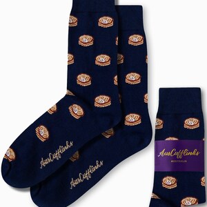 May include: Navy blue socks with a repeating pattern of brown and tan meat pies. The socks have the text "AusCufflinks" in a cursive font. A pair of socks and a single sock are displayed.