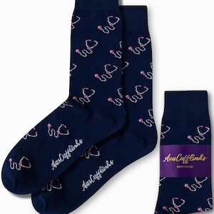 Puede incluir: Un par de calcetines azul marino con un patrón de estetoscopio blanco y rosa. Los calcetines tienen el texto "AusCufflinks" en el lateral. Los calcetines están empaquetados con una etiqueta que dice "AusCufflinks AUSTRALIA".