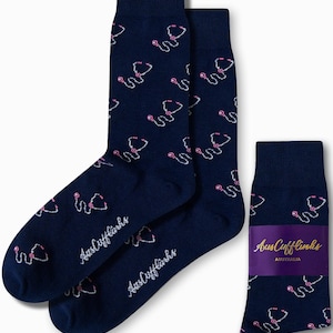Könnte beinhalten: Marineblaue Socken mit einem sich wiederholenden Muster aus rosa und weißen Stethoskopen. Die Socken tragen den Schriftzug "AusCufflinks" in weißer Schrift. Ein gefaltetes Paar Socken wird ebenfalls mit einem lila Band mit dem Text "AusCufflinks AUSTRALIA" gezeigt.