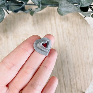 May include: A gray heart-shaped cookie cutter made of plastic. The cutter is layered with multiple heart shapes.