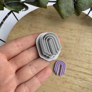 May include: A set of three silver metal cookie cutters shaped like arches, with a smaller purple arch cookie cutter in the background.