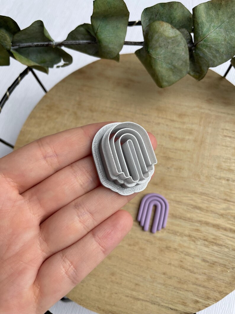 May include: A set of three silver metal cookie cutters shaped like arches, with a smaller purple arch cookie cutter in the background.