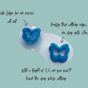 May include: Two blue plastic butterfly cookie cutters. The cutter on the left has a wide edge for easier cutting. The cutter on the right has a thin cutting edge to prevent clay from sticking. The text "With a Hight of 1,4 cm you won't Touch the clay while cutting" is written below the cutters.