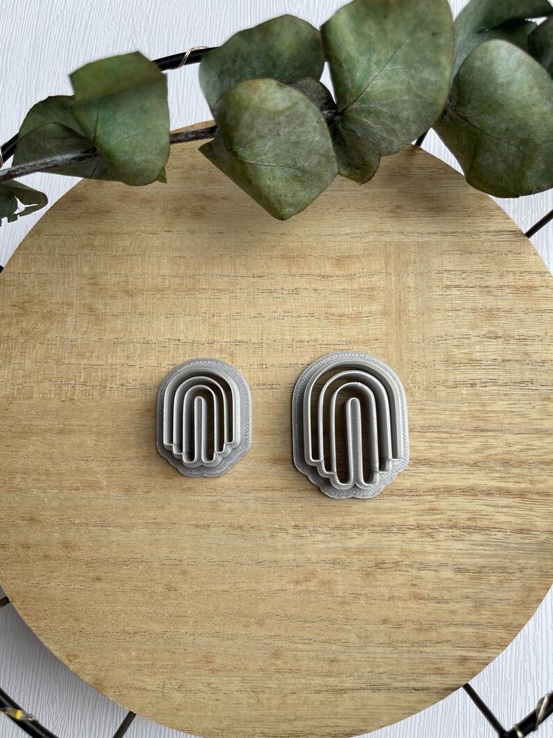 May include: Two silver cookie cutters shaped like arches, one larger than the other, on a wooden surface.
