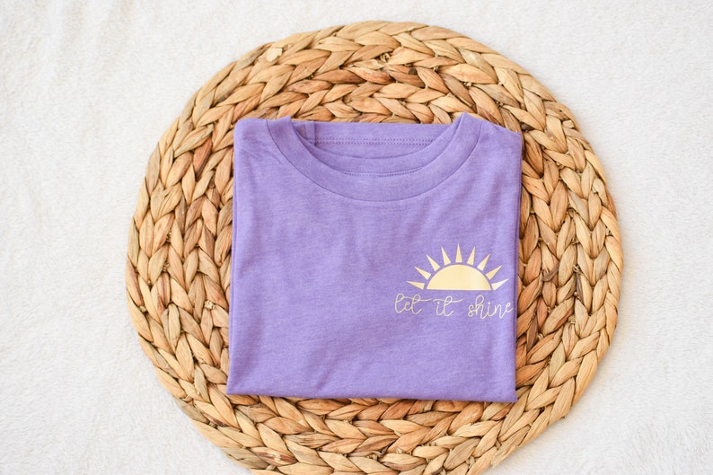 May include: A purple t-shirt with a gold sun graphic and the text "Let it shine".