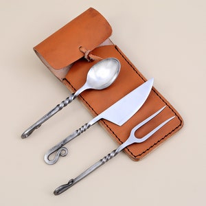 Könnte beinhalten: Ein Set aus drei silbernen Besteckteilen, einem Löffel, einem Messer und einer Gabel, mit gedrehten Griffen, in einer braunen Lederscheide.