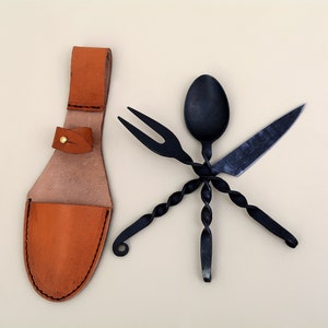 Könnte beinhalten: Ein Set aus schwarzem, geschmiedetem Besteck aus Metall, bestehend aus Messer, Gabel und Löffel, mit einem gedrehten Design. Das Besteck ist sternförmig angeordnet und wird von einer braunen Lederscheide begleitet.