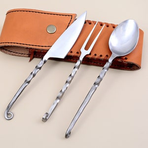 Könnte beinhalten: Ein Set aus drei gedrehten Metallbesteckteilen, bestehend aus Messer, Gabel und Löffel, wird in einer braunen Lederscheide präsentiert. Das Besteck hat ein einzigartiges gedrehtes Design und ist aus poliertem Metall gefertigt.