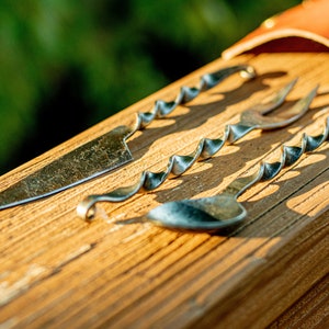 Könnte beinhalten: Ein Set aus drei silbernen Besteckteilen mit gedrehten Griffen. Das Besteck umfasst ein Messer, eine Gabel und einen Löffel. Das Besteck liegt auf einer Holzoberfläche.