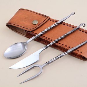 Könnte beinhalten: Ein Set aus drei silbernen Besteckteilen, ein Löffel, ein Messer und eine Gabel, mit gedrehten Griffen, werden in einer braunen Lederscheide gezeigt.