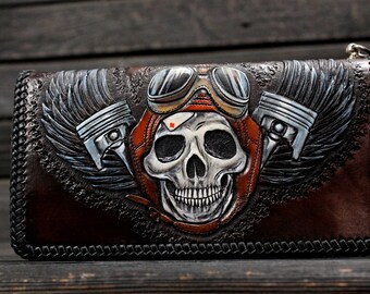 May include: A brown leather wallet with a tooled design of a skull wearing goggles and an aviator helmet with wings and pistons on either side.