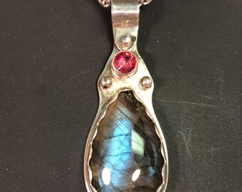 Puede incluir: Un collar de plata con un colgante en forma de lágrima con una piedra de labradorita y un pequeño acento de piedra rosa.