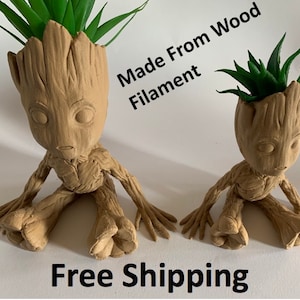Puede incluir: Dos macetas Groot de madera impresas en 3D de color marrón con plantas verdes. El texto "Made From Wood Filament" está escrito en el lado derecho de la imagen. El texto "Free Shipping" está escrito en la parte inferior de la imagen.