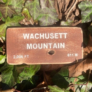 May include: A brown wooden sign with white text that reads "WACHUSETT MOUNTAIN" with the elevation listed as "2,006 FT" and "611 M".