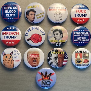 May include: A collection of round political buttons with various anti-Trump slogans and images. The buttons feature phrases like "Impeach Trump," "Fuck Trump," and "No Kings." Some buttons have images of Barron Trump and a cat.