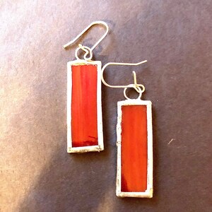May include: A pair of red rectangular stained glass earrings with silver frames and hooks.