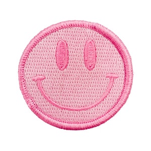 May include: Pink embroidered smiley face patch. The patch is round and has a white background with pink stitching.